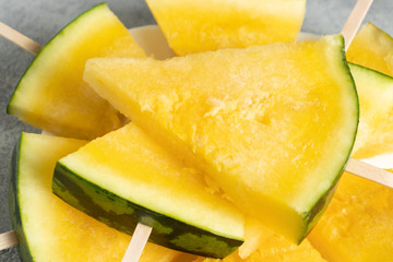 Slices of yellow watermelon on wooden sticks on a dish on the table closeup