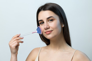 Close-up of a young girl in a light top on a white background making a facial make-up. A pretty...
