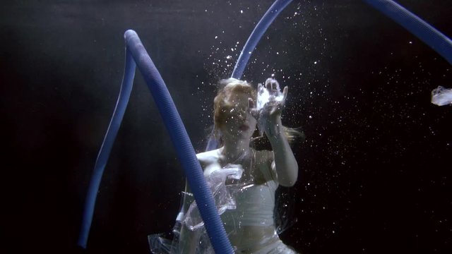 slim blonde woman swims deep underwater among polyethylene