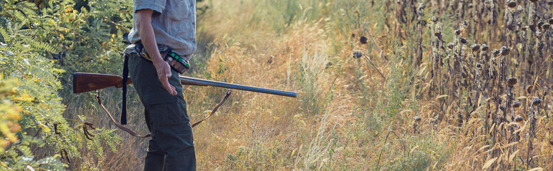A man with a gun in his hands and an green vest  on a pheasant hunt in a wooded area in cloudy...