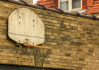 A lonely vintage backyard basketball net on a brown brick wall above a garage door- wanting to be played with again.