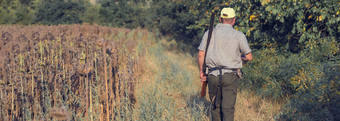 A man with a gun in his hands and an green vest  on a pheasant hunt in a wooded area in cloudy...