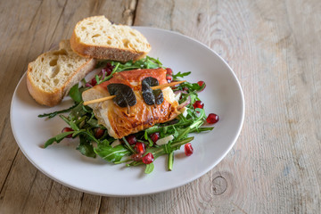Roasted chicken saltimbocca wrapped with prosciutto ham and sage leaves served with bread on arugula salad on a white plate on a rustic wooden table, copy space