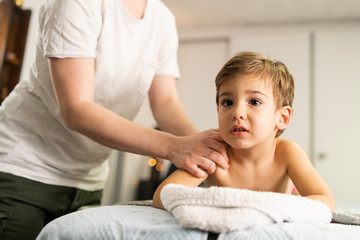 Fototapeta premium Small caucasian boy laying on the bed naked having back massage by professional female physiotherapist masseuse in a rehabilitation center salon or home office of physical therapy