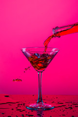 Droplets of Drink Spilling Out of The High Glass Goblet with Ice Cubes and Colorful Liquid. Isolated Over Colorful Background.