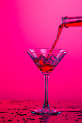Droplets of Drink Spilling Out of The High Glass Goblet with Ice Cubes and Colorful Liquid. Isolated On Colorful Background.