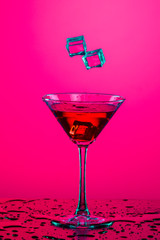 Two Ice cubes Falling to High Glass Goblet with Ice Cube and Red Liquid. Over Colorful Background.