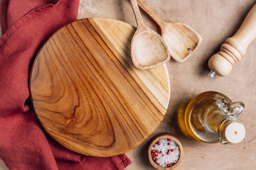 Wooden cutting board over towel with utensils on beige rustic kitchen table. Space for your recipe or menu. Top view.