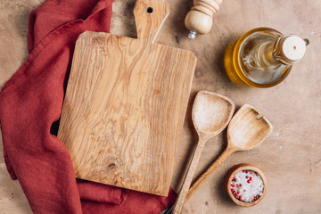 Wooden cutting board over towel with utensils on beige ructic kitchen table. Space for your recipe or menu. Top view.
