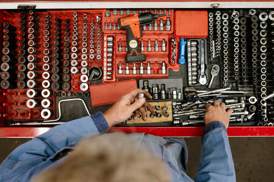 High angle view of mechanic selecting tool from toolbox in automobile workshop