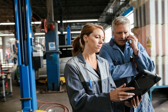 Female Car Mechanic Using Digital Tablet And Talking To Colleague In Garage