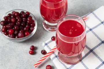 Two glasses with homemade freshly cranberry juice and a bowl of cranberries on a gray concrete table