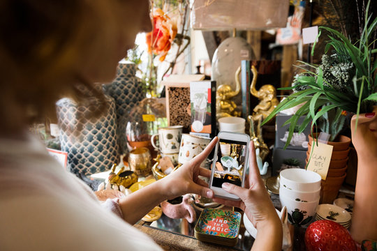Young woman taking photo of merchandise in gift shop on smart phone