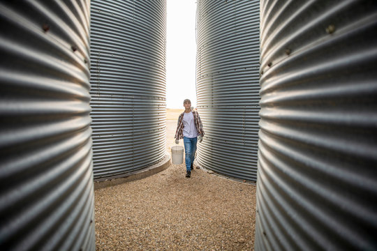 Teenage boy farmer carrying bucket between silos