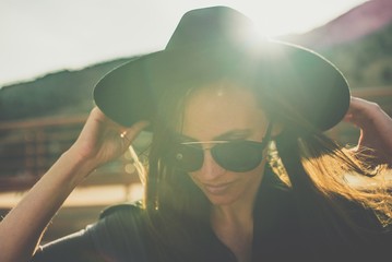 A woman wearing a black hipster hat in front of a sunset over the mountain