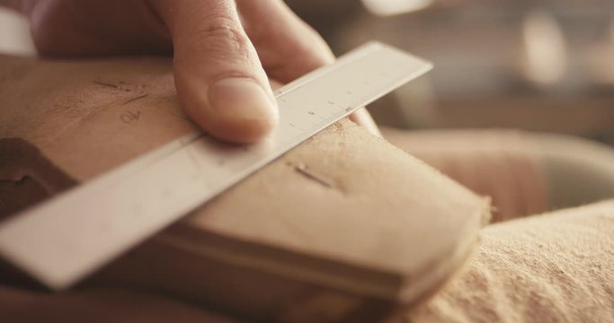 Traditional bespoke shoemaker measuring marking leather insole on wooden shoe last with ruler pencil closeup