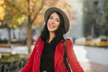 Cute brunette woman standing in park with happy smile. White stylish girl laughing while walking in september day.