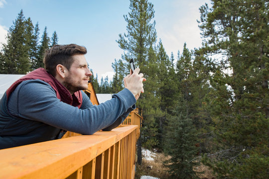 Man using camera phone on cabin balcony in woods