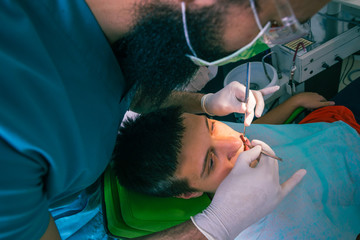 The dentist is examining teenage boy's teeth in the dentist chair in the dental office
