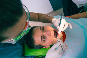 The dentist is examining teenage boy's teeth in the dentist chair in the dental office