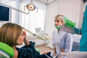 Close up portrait of a beautiful young lady sitting in the dental chair while stomatologist ( dentist ) with hands in sterile gloves is fixing her teeth.