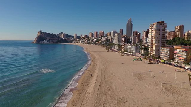 Aerial journey flying along the popular Spanish Mediterranean beach resort town Benidorm with high rise complexes  