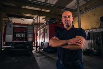 Portrait of handsome firefighter standing against trucks at fire station
