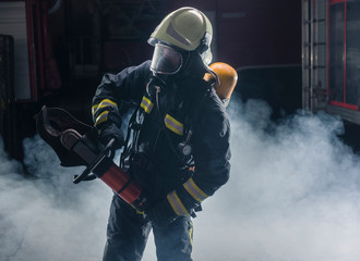 Portrait of a fireman wearing firefighter turnouts and helmet. Dark background with smoke and blue light.