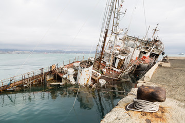 An old fishing boat sunk at a pier in seaport