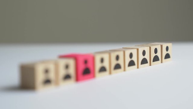 Hand picking up a red icon people cube among the rest of cubes for hiring the right candidate concept. Focus point is moving slowly toward the red color square block.