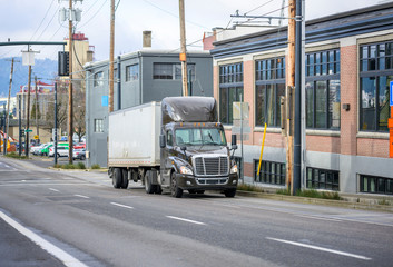 Big rig dark brown day cab semi truck transporting cargo in short dry van semi trailer running on...