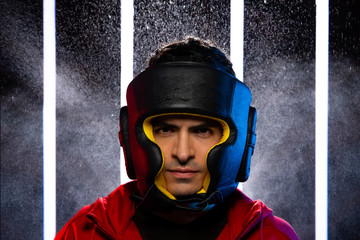 Close up look at camera of Athlete Caucasian Strong Man is putting Black Leather Head Guard Gear. Office male wears Red Hood Jacket in Neon Muay Thai Boxing Gym, copy space sweat water splash in Air