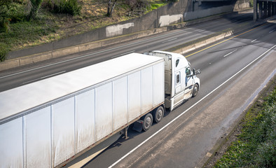 Dirty after rain big rig semi truck with dry van semi trailer running on the wide multilines...