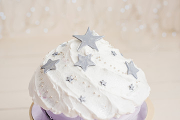 A magical beautiful holiday cake made of gray stars, white cream and lilac biscuit. Birthday gift. Birthday party. Shiny wall background made of small led lamps.