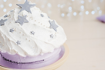A magical beautiful holiday cake made of gray stars, white cream and lilac biscuit. Birthday gift. Birthday party. Shiny wall background made of small led lamps.