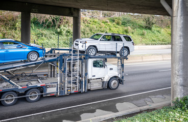 Powerful big rig car hauler semi truck transporting cars on semi trailer running under the bridge...