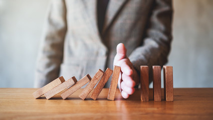 Closeup image of a businessman's hand try to stopping falling wooden dominoes blocks for business...