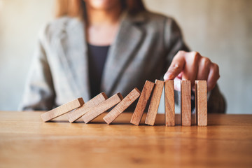 Closeup image of a businesswoman's finger try to stopping falling wooden dominoes blocks for...