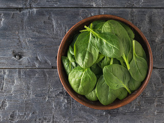 A clay bowl filled with spinach leaves on a black wooden table. Food for fitness. The view from the top.