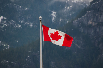 A picture of Canada flag waving against the mountain lightly dusted with snow.   Squamish BC Canada