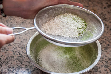 Flour being sifted into a stainless steel container.A girl sieving flour in bowl in kitchen. The flour is using for making bread.