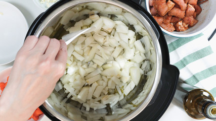 Saute chopped onion in a multicooker. Cooking rice with meat and vegetables  in pressure multi cooker step by step, top view.