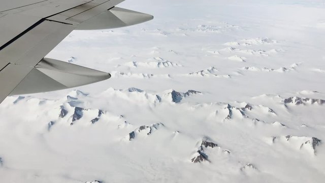 Flying over Greenland's arctic landscape with airplane wing view