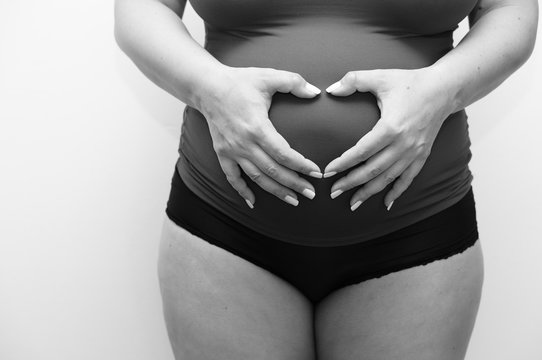 Grayscale Shot Of A Pregnant Woman With Her Hands On Her Womb Creating A Heart Shape