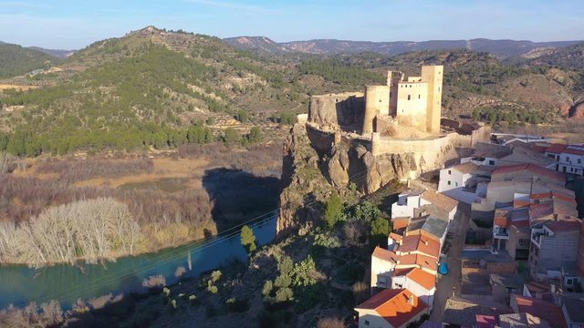 Aerial panoramic view of medieval partially restored Cofrentes castle above the Cabriel river in Spain with reflection and dramatic sky