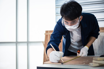 Asian man Carpenter working with technical drawing or blueprint construction paper lying on a workshop with carpentry tools and wood at home