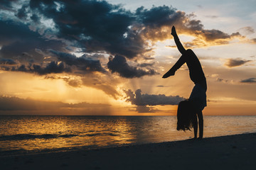 A woman doing a graceful handstand on the beach in silhouette 