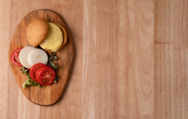 Top view of fresh tasty homemade hamburger with fresh vegetables, lettuce, tomato, cheese beside sliced tomatoes on a cutting board. Free space for text