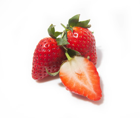 three strawberries, one half and two whole ones behind it, are isolated on a white background