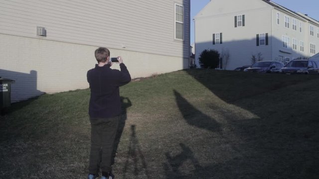 young man walks up and takes a picture of the side of a house.